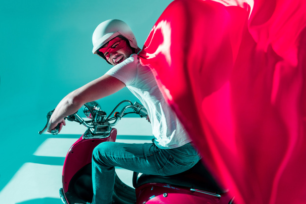 side view of man in protective helmet and superhero costume on red scooter - Fotoğraf, Görsel