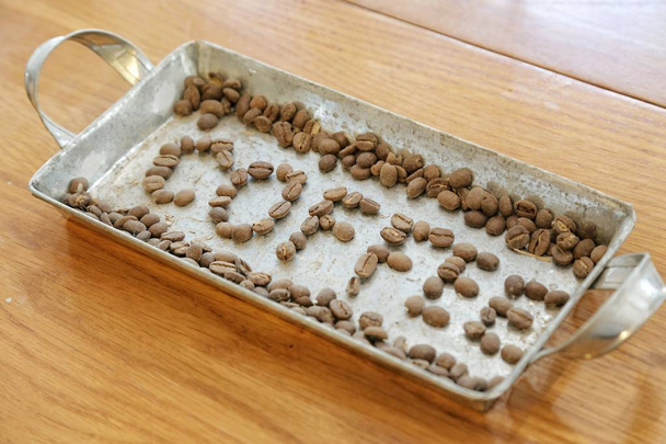 organizar granos de café para hacer la palabra café en una bandeja de acero inoxidable sobre una mesa de madera
 - Foto, Imagen