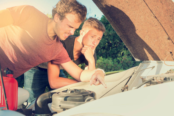 Хлопці дивляться на зламану машину
 - Фото, зображення