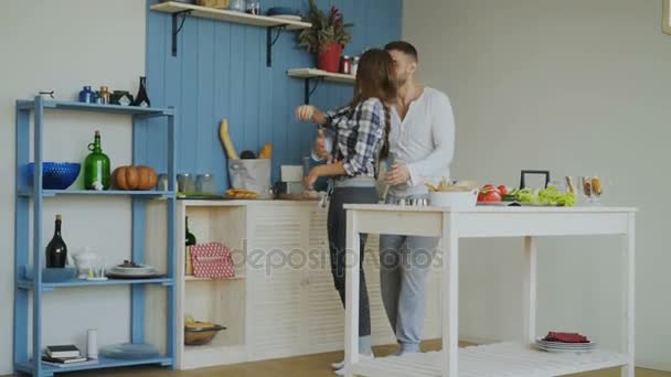 Joyful and attractive young couple in love dancing together and have fun in the kitchen at home on holidays - Video, Çekim