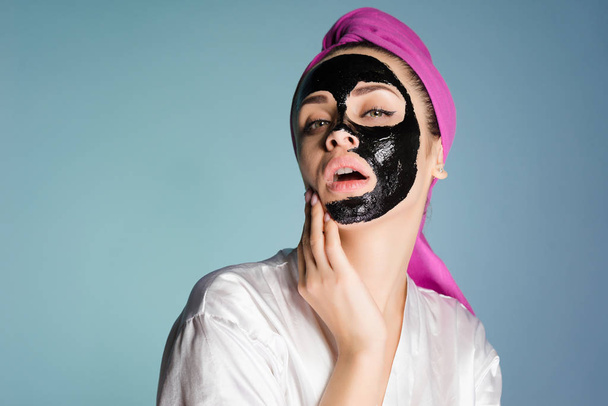 attractive young girl with a pink towel on her head, on her face a black cleansing mask - Fotoğraf, Görsel