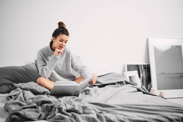 Girl sitting on bed and reading book in the morning - Photo, Image