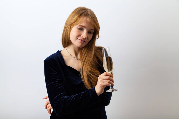 young elegant lady with red hair and freckles dressed in dark velvet dress holding glass of champagne and thoughtfully looking aside  - 写真・画像