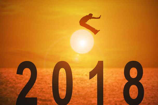Sylwetka młodego człowieka, skoki nad liczbami 2018 roku z piękny zachód słońca nad morzem, koncepcje news roku i biznes cel. - Zdjęcie, obraz
