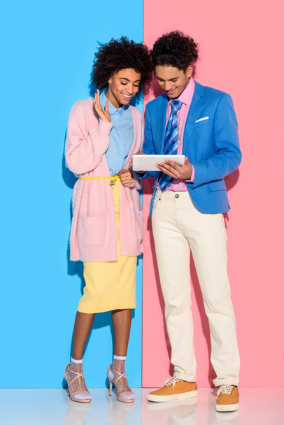Smiling couple using digital tablet on pink and blue background  - Fotó, kép