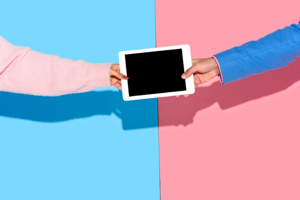 Cropped image of hands holding digital tablet on pink and blue background - 写真・画像