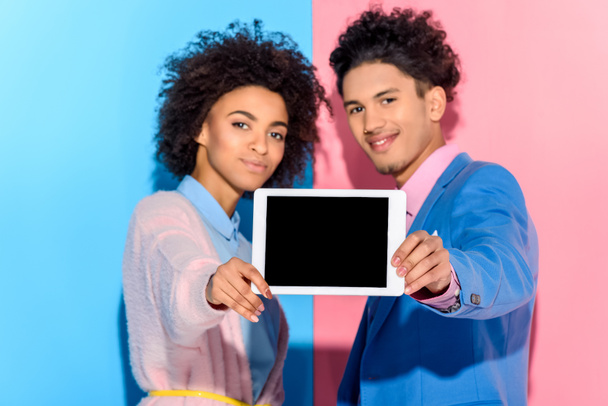 Smiling couple holding digital tablet in hands on pink and blue background - Foto, imagen