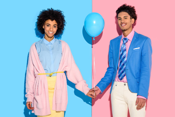 Young couple holding hands with air balloon on pink and blue background - Foto, afbeelding