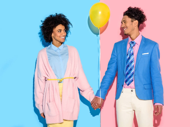 Smiling couple holding hands with air balloon on pink and blue background - Valokuva, kuva