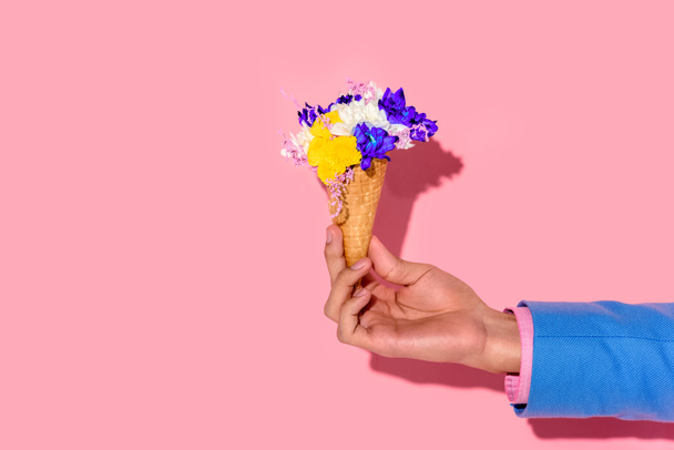 cropped shot of african american man holding flowers in ice cream cone on pink wall background - Фото, изображение