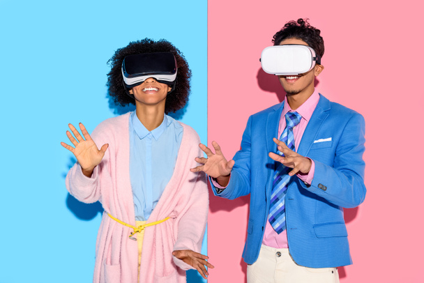 portrait of african american couple in vr headsets against pink and blue wall background - Photo, Image