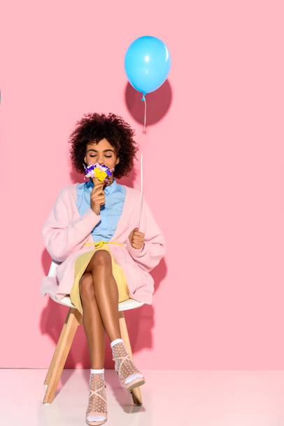 african american woman with flowers in ice cream cone and balloon in hands on pink wall backdrop - Φωτογραφία, εικόνα