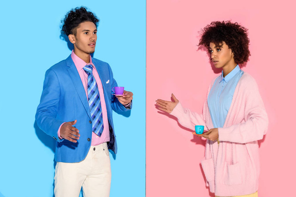 Elegante pareja afroamericana con tazas de té de juguete con fondo de pared rosa y azul
 - Foto, imagen