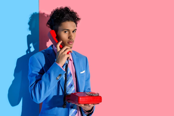 portrait of stylish african american man talking on retro telephone against pink and blue wall - Photo, Image
