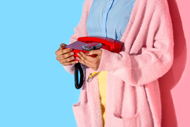 visão parcial da mulher afro-americana segurando telefone retro em mãos com fundo de parede rosa e azul
 - Foto, Imagem
