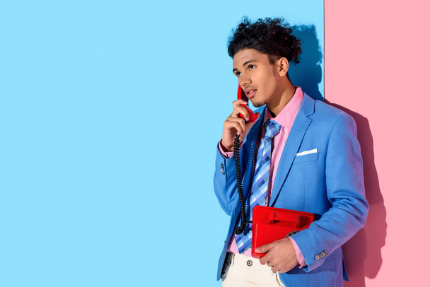 handsome man using handset of retro phone on pink and blue background - Photo, Image