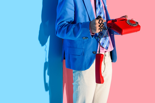 Midsection of man in formal suit with retro phone in hands on pink and blue background - Photo, Image
