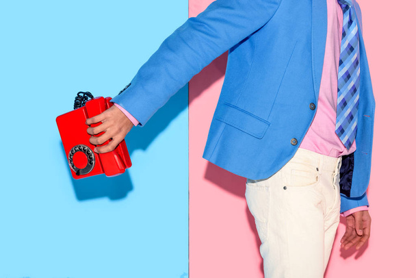 Midsection of young man in jacket with retro phone in hand on pink and blue background - Photo, Image