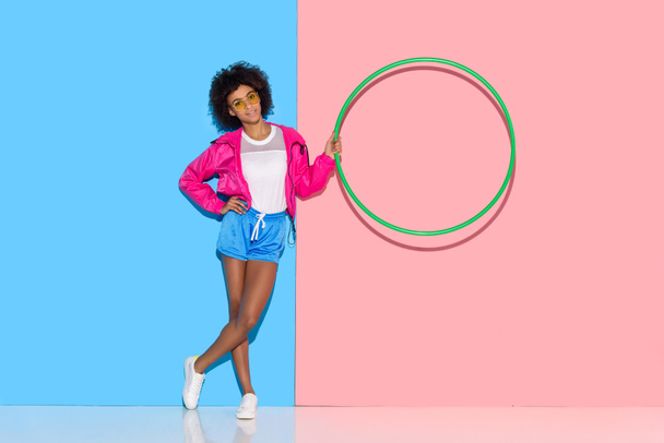 Woman in sportswear standing with hoop in hand on pink and blue background  - Foto, immagini
