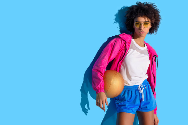  バスケット ボール ボールを押し、青の背景によそ見のメガネの少女    - 写真・画像