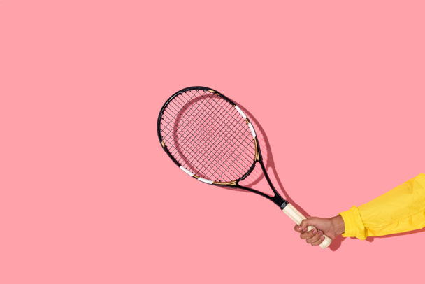 Close-up beeld van mannelijke hand hebt tennisracket op roze achtergrond  - Foto, afbeelding