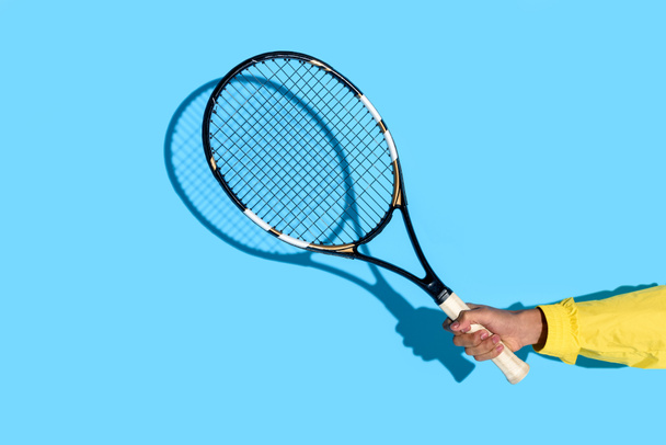Close-up view of male hand holding tennis racket on blue background  - Zdjęcie, obraz