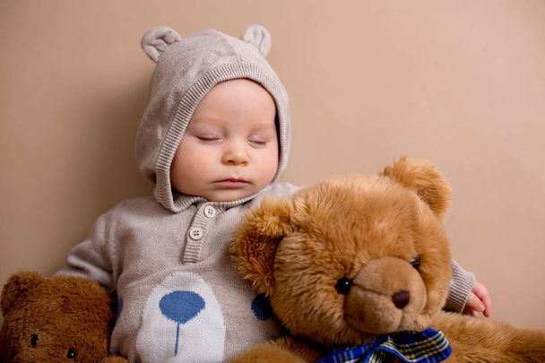 Sweet baby boy in bear overall, sleeping on a shelf with teddy b - Photo, image