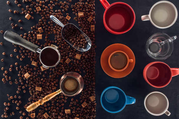 top view of roasted coffee beans, scoop, coffee pot, coffee tamper and cup of coffee with empty cups on black - 写真・画像