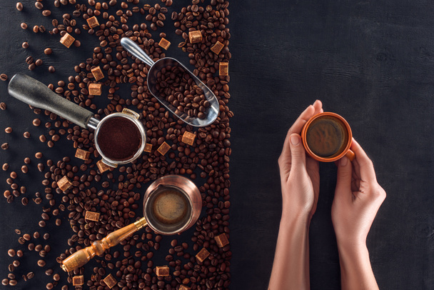 vue du dessus de la personne tenant tasse de café et grains de café torréfiés avec cafetière, cuillère et sucre
 - Photo, image