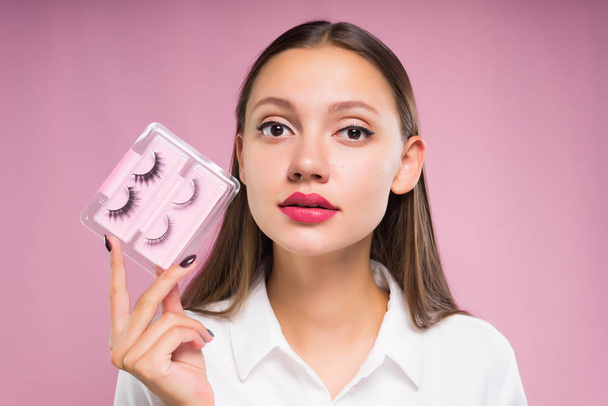 young girl holding a set of false eyelashes on a pink background - Foto, afbeelding