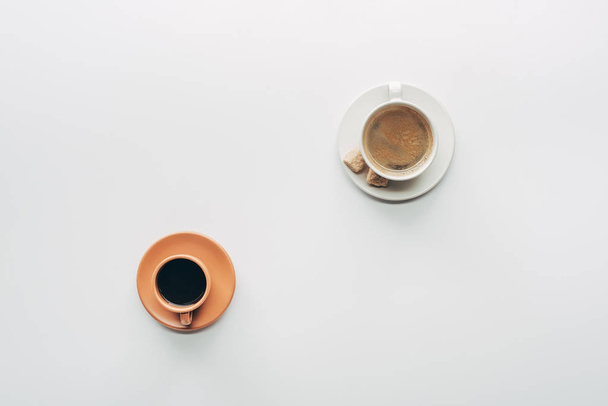pohled shora na dva šálky kávy s podšálky a hnědého cukru izolované na bílém  - Fotografie, Obrázek