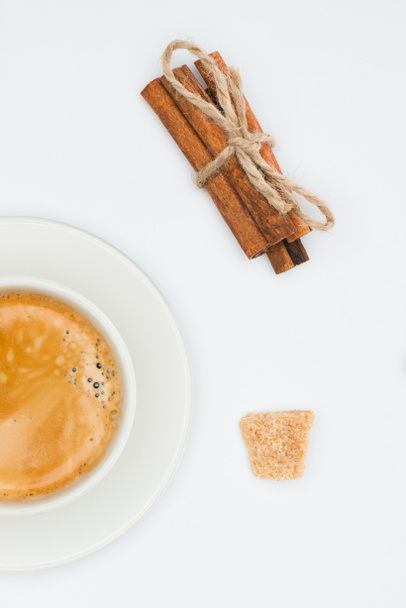 top view of cup of coffee with saucer, brown sugar and cinnamon sticks with rope isolated on white - Photo, Image