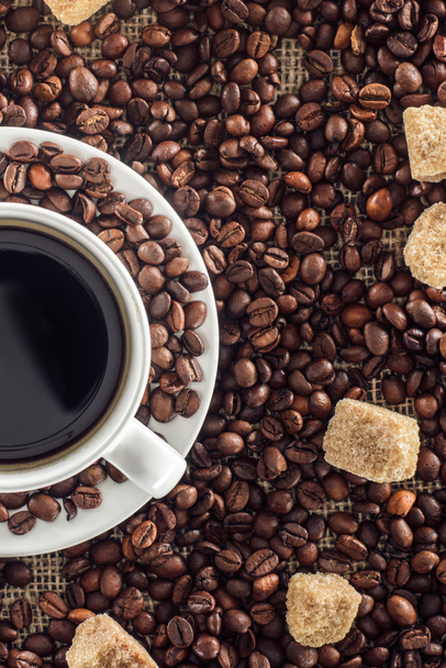 vergrote weergave van kopje koffie, gebrande koffiebonen en bruine suiker op zak   - Foto, afbeelding