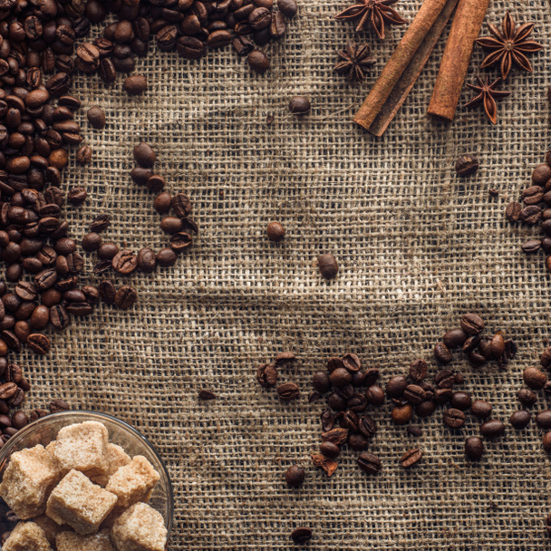 vue du dessus des grains de café torréfiés avec bâtonnets de cannelle et sucre brun dans un bol en verre sur sac
  - Photo, image