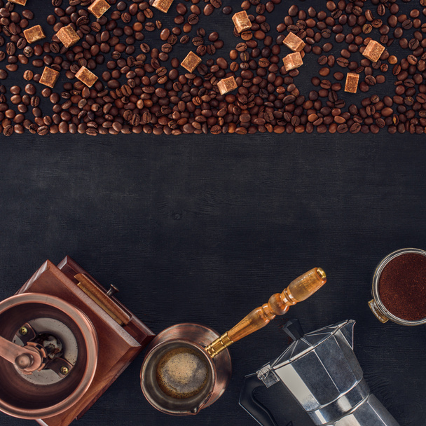 top view of roasted coffee beans, scoop, coffee grinder, coffee pot and coffee maker on black   - Foto, afbeelding