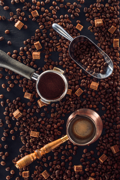 vista superior de granos de café tostados, cucharada, manipulador de café, cafetera y azúcar morena en negro
  - Foto, Imagen