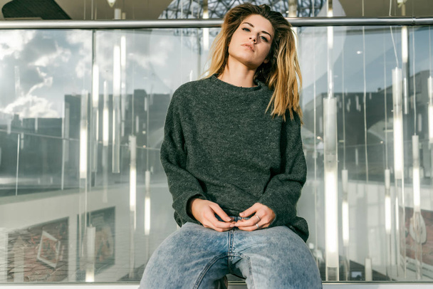 young girl in gray-green sweater sits leaning against glass barrier - Foto, imagen