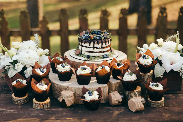 hoekmening van berry taart en cupcakes met bosbessen en rozemarijn op houten stronken - Foto, afbeelding