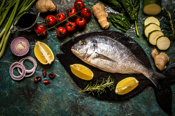 Dorada fish with vegetables, lemon, spices and greens on a blue background - Photo, Image