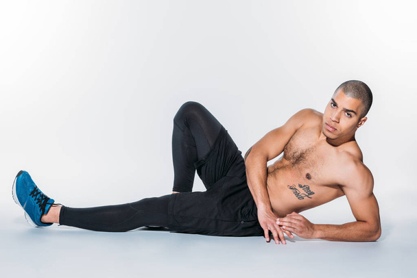 shirtless tattooed african american sportsman lying on floor and looking at camera - Foto, Imagem