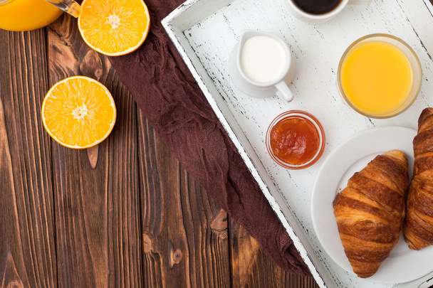 Croissant recién horneado, zumo de naranja, frutas frescas, mermelada sobre fondo de madera marrón. Desayuno francés. Pasteles frescos para la mañana. Delicioso postre. Vista superior. Fotografía de cerca. Banner horizontal
 - Foto, imagen