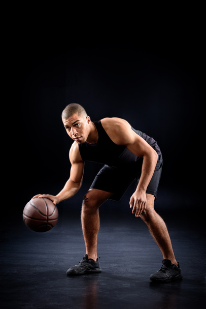 african american basketball player bouncing ball on black - Foto, afbeelding