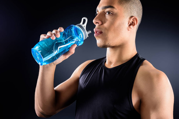 handsome african american sportsman drinking water on black - Фото, изображение