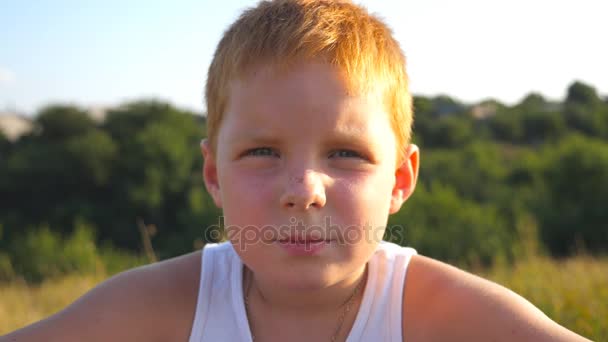 Młody rude włosy chłopak z piegami, patrząc na kamery z poważną miną na twarzy na zewnątrz. Portret smutny dzieci z emocji i uczuć. Slow motion z bliska - Materiał filmowy, wideo