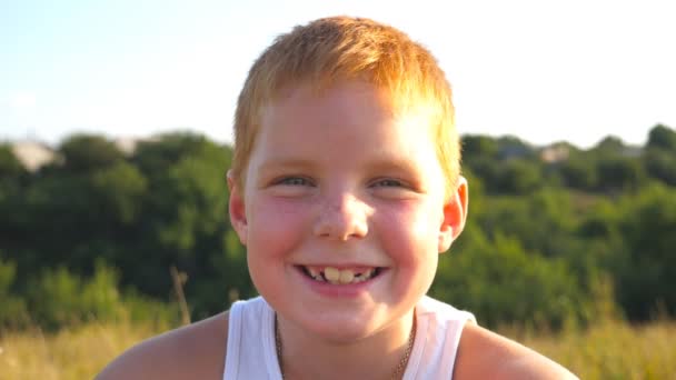 Portrait of happy red hair boy with freckles laughs outdoor. Adorable handsome baby looking into camera with joyful smile. Close up emotions of male child with glad expression on face. Slow motion - Footage, Video