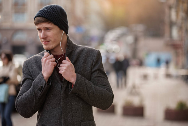 Elegant young man with earphones walking in the city - Photo, image