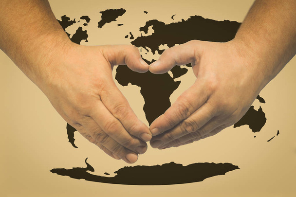 Εορτασμός της ημέρας της γης - τα χέρια σε σχήμα καρδιάς που σχετίζονται με ένα χάρτη του κόσμου  - Φωτογραφία, εικόνα