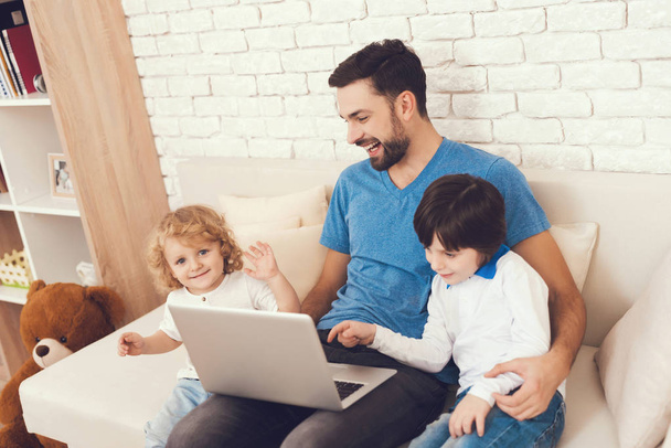 A man spends time with his sons. The father of two boys is engaged in raising children. Father teaches children about technology. The man shows his sons how to work with the laptop. - 写真・画像