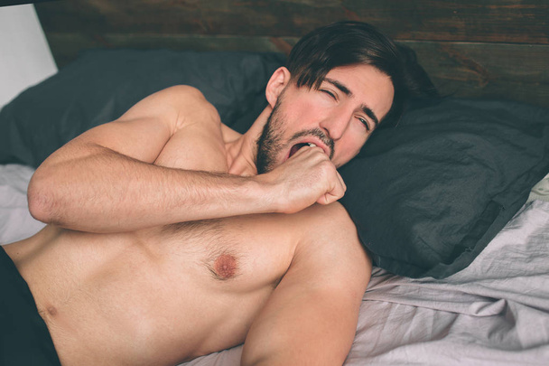 Carefree guy enjoying new day. Sexy, happy bearded man in bed - 写真・画像