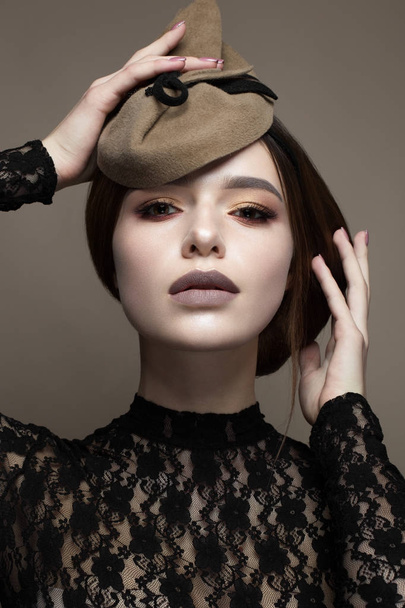 A young girl in an unusual hat and an elegant hairdo. Beautiful model with a gentle make-up in chocolate shades. Retro image. Beauty of the face. Photo taken in the studio. - Photo, image